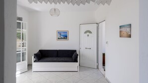 Una habitación con una puerta blanca, un sofá de color oscuro, un cuadro en la pared y una lámpara colgante.