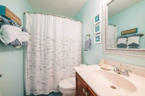 Une salle de bain avec un rideau de douche blanc, un lavabo avec un miroir et des serviettes accrochées au mur.