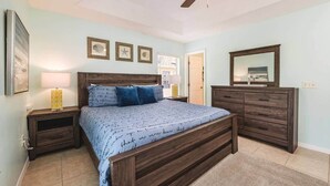 Een slaapkamer met een houten bed, nachtkastjes, een dressoir en een plafondventilator.