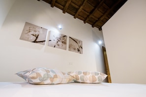 Quarto com teto de madeira, cama com almofadas estampadas e três quadros de flores pendurados na parede.
