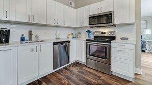 A modern kitchen with white cabinets, stainless steel appliances, and a wooden floor. - Tropical Beach Bungalow Up | 3 bedrooms | Across Street from Beach | Deck (Fernandina Beach)