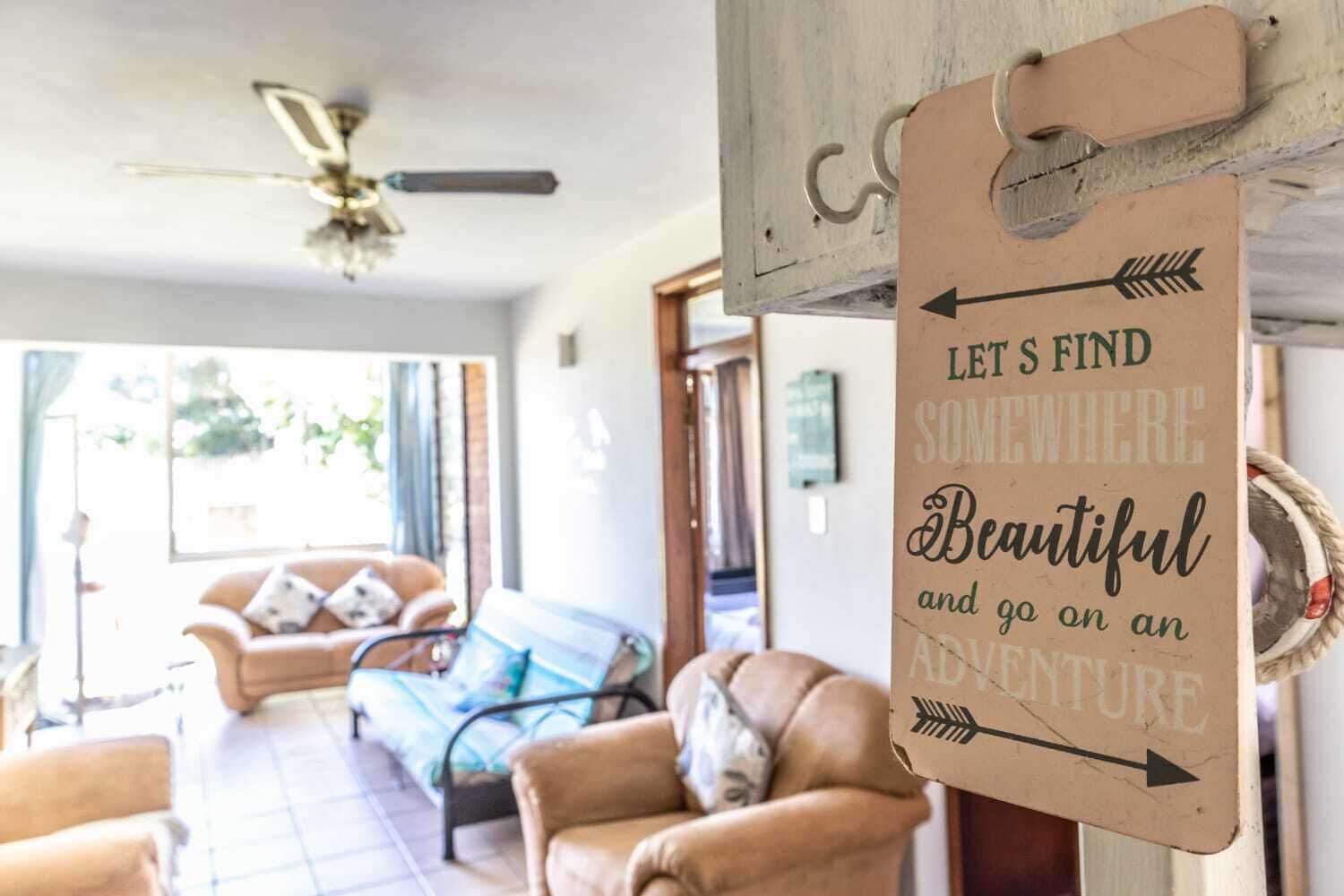 A cozy living room with a sofa, armchairs, and a coffee table. A sign on the wall reads "Let's find somewhere beautiful and go on an adventure."