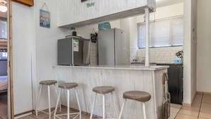 A kitchen area with a white countertop, four stools, a refrigerator, and a sink. - Sunny Tides Holiday Inn (Kingsburgh)