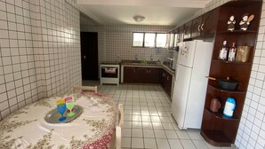 A kitchen with white tiled walls, a dining table with a floral tablecloth, and a wooden cabinet with kitchen items. - Calypso solar building A gated community in Atalaia close to the beach. (salinopolis)
