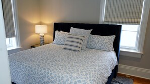Una cama bien hecha con una colcha de estampado geométrico, un cabecero negro y dos lámparas de noche.