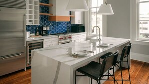 Una cocina moderna con una isla central, armarios blancos, un salpicadero azul hexagonal y un ventanal que proporciona luz natural.