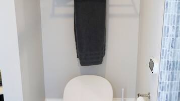 Un bagno con il water, un porta asciugamani con asciugamani piegati, un portasciugamani bianco e un box doccia in vetro.