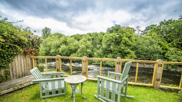 A deck with two rocking chairs and a small table, overlooking a river and surrounded by lush greenery. - Cornerstones - 16th Century House overlooking River in Llangollen (LLANGOLLEN)