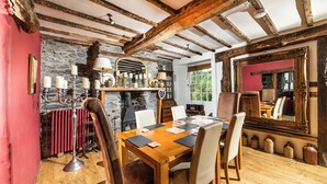 A dining area with a wooden table, chairs, a stone wall, and a fireplace. - Cornerstones - 16th Century House overlooking River in Llangollen (LLANGOLLEN)