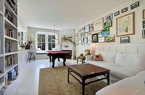A living room with a pool table, white sofas, a bookshelf, and a wall decorated with framed pictures.