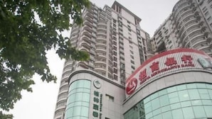 A multi-story building with a curved glass facade, a prominent red sign, and several parked cars in front. - Greentree Jiangsu Suzhou Shilu Walk Street West Ganjiang Road Shell Hotel (Suzhou)