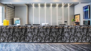 A modern hotel reception area with a marble counter, a digital screen, and a plant. - Greentree Jiangsu Suzhou Shilu Walk Street West Ganjiang Road Shell Hotel (Suzhou)