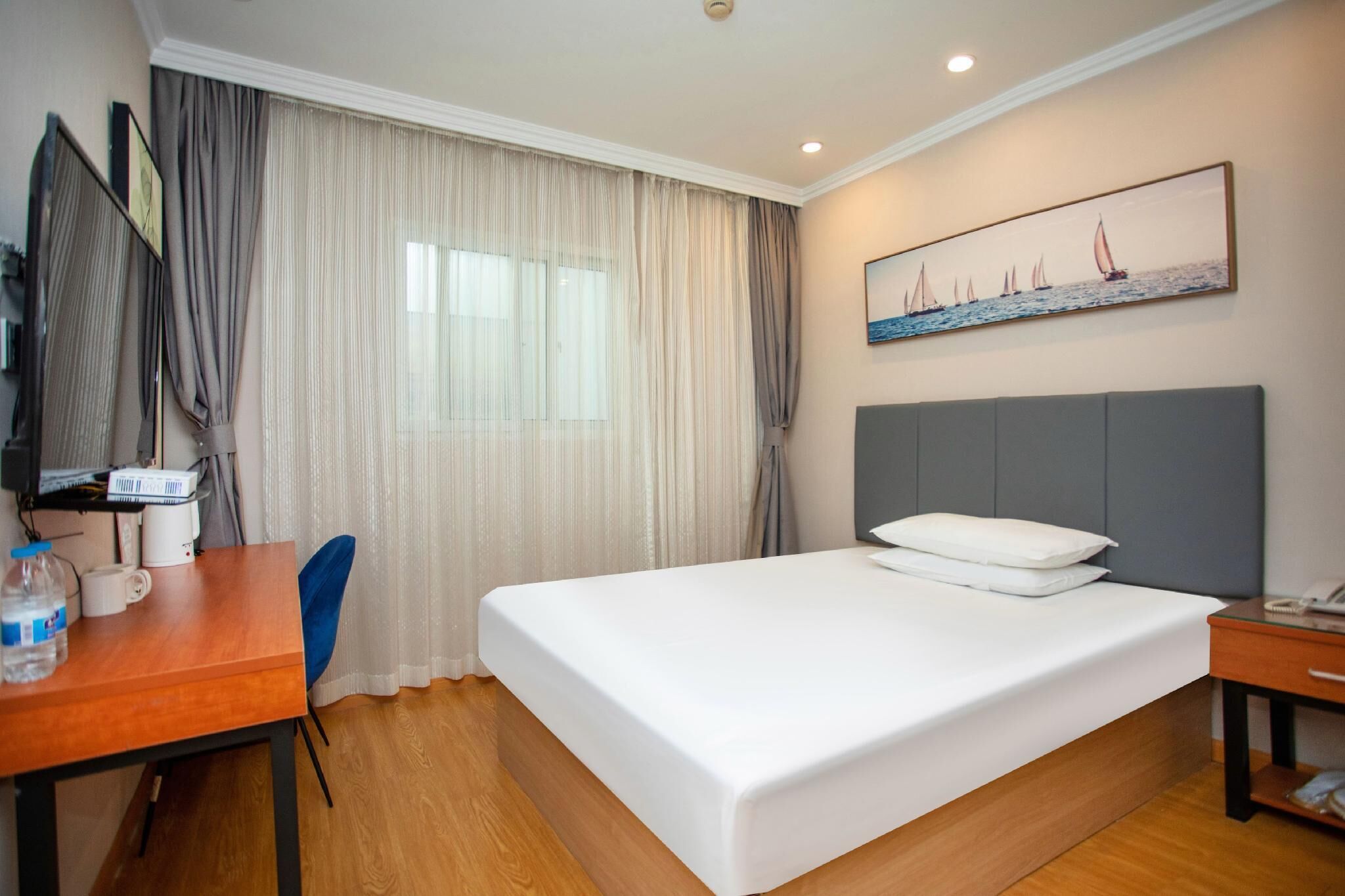 Habitación de hotel con una cama grande, un escritorio con silla, una mesita y un cuadro en la pared.