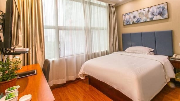 A hotel room with a bed, a desk with a computer, a plant, and a window with curtains. - Greentree Jiangsu Suzhou Shilu Walk Street West Ganjiang Road Shell Hotel (Suzhou)