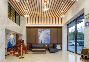 A modern lobby with a reception desk, seating area, and a large window offering a view of the street.