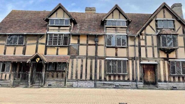 Un edificio tradicional con entramado de madera y una fachada simétrica, con varias ventanas con persianas y una entrada protegida por una reja.
