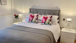 Un dormitorio ordenado con una cama grande, dos mesitas de noche, una lámpara colgante y un radiador.