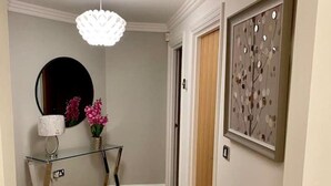 Un pasillo con una mesa consola de vidrio, un espejo redondo, una puerta de madera y una obra de arte enmarcada en la pared.