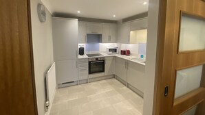Una cocina compacta con armarios blancos, microondas, tostadora y lavamanos.