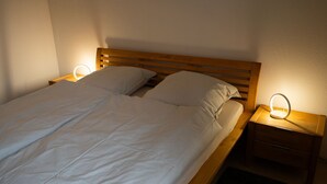 A double bed with a wooden headboard, two pillows, and a bedside table with a built-in lamp.