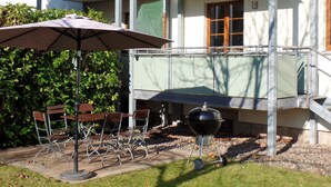 An outdoor patio with a grill, chairs, and an umbrella.