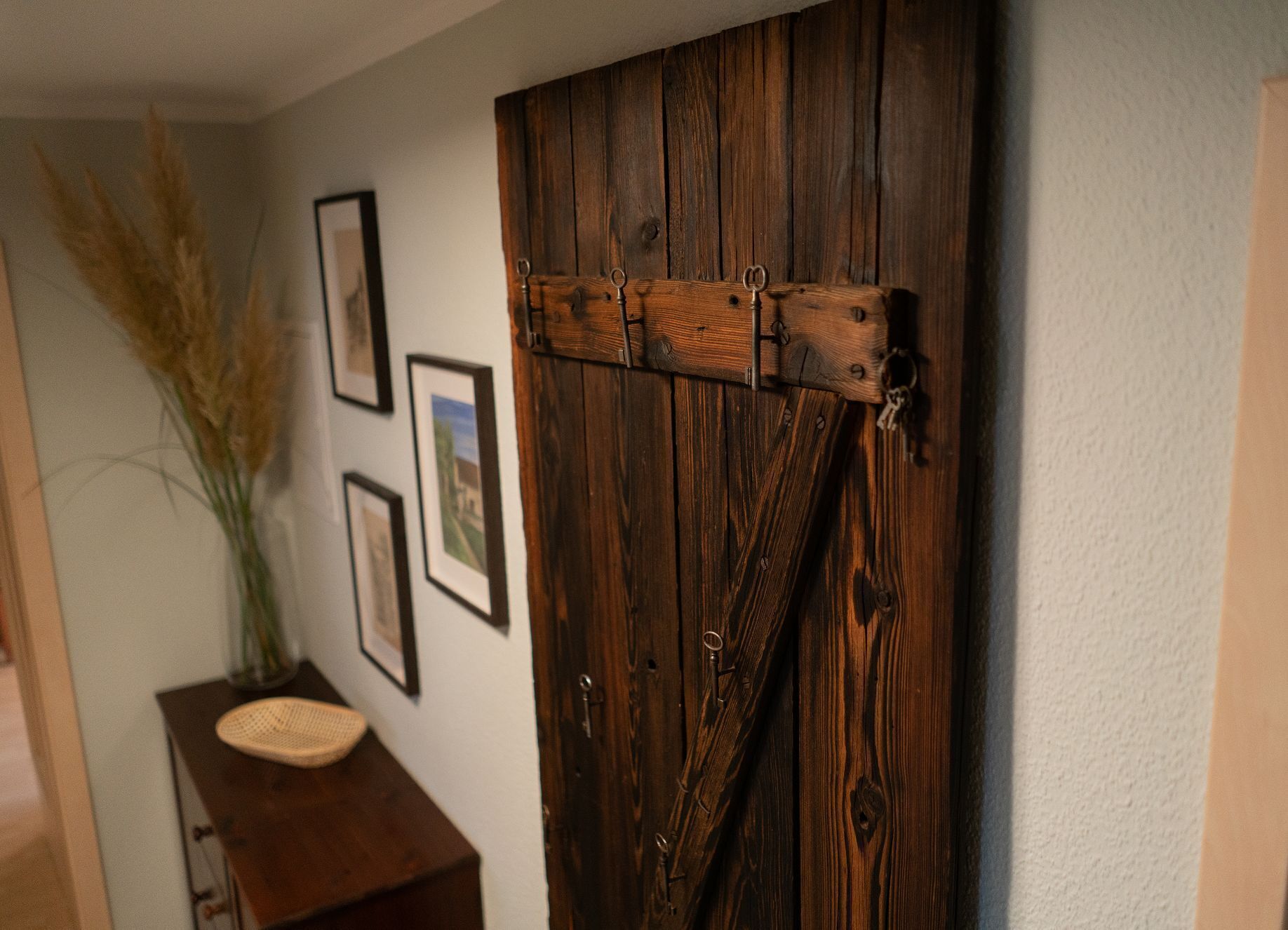 Eine rustikale Holztür mit Metallscharnieren und Riegel, ein gerahmtes Bild an der Wand und ein kleiner Tisch mit einem gewebten Korb.
