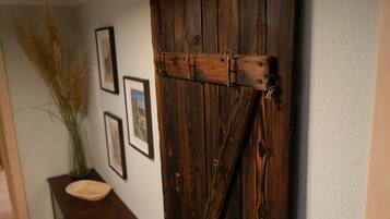 Eine rustikale Holztür mit Metallscharnieren und Riegel, ein gerahmtes Bild an der Wand und ein kleiner Tisch mit einem gewebten Korb.