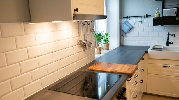 A modern kitchen with white subway tiles, a black stovetop, wooden cutting board, and white cabinets.