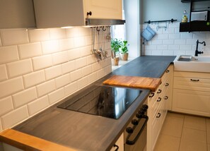 A modern kitchen with white subway tiles, a black stovetop, wooden cutting board, and white cabinets. - Family-friendly vacation apartment Elbtal-Apartment.de (Heidenau)
