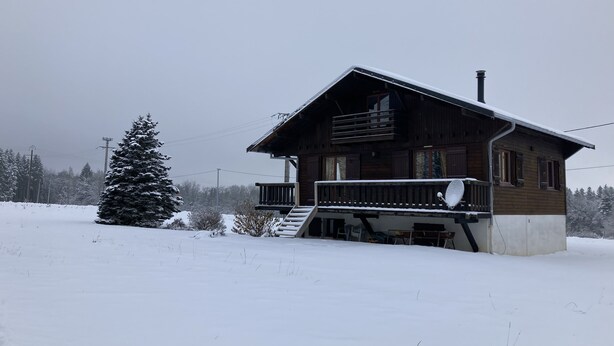 Una cabaña de madera con balcón, rodeada de nieve y árboles.