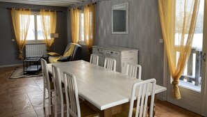 Un comedor con una mesa y sillas blancas, un radiador y una ventana con cortinas amarillas.