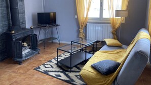 Una sala de estar con chimenea, un sofá, un televisor sobre un mueble bajo y cortinas amarillas.