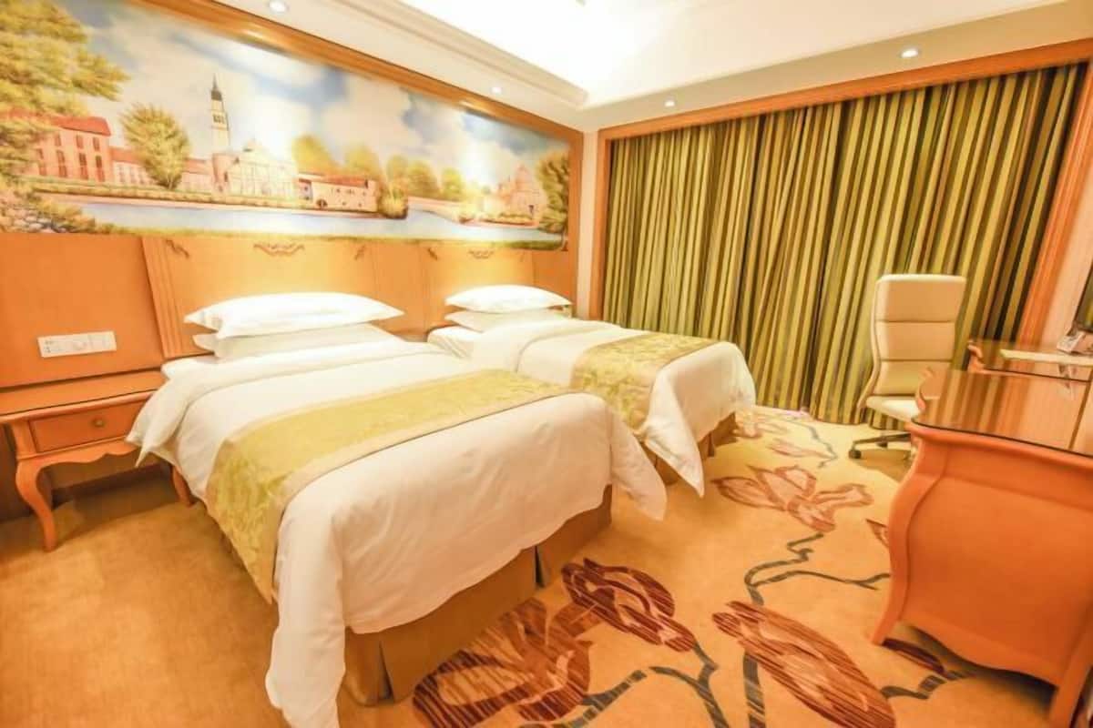 A hotel room with two beds, a desk, and a chair.