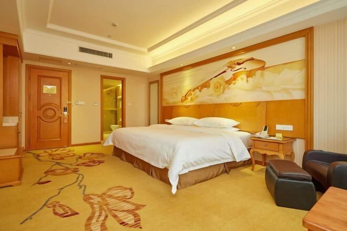 A hotel room with a large bed, a desk, a chair, and a carpet with a floral pattern.