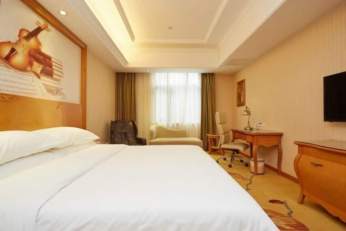 A hotel room with a large bed, a desk, a chair, a television, and a window with curtains.