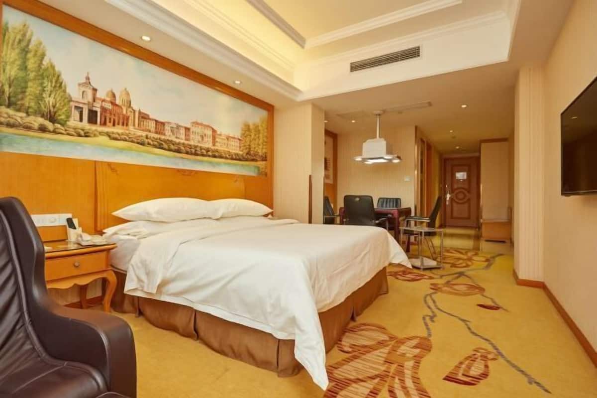 A hotel room with a bed, a desk, a chair, a TV, and a painting on the wall.