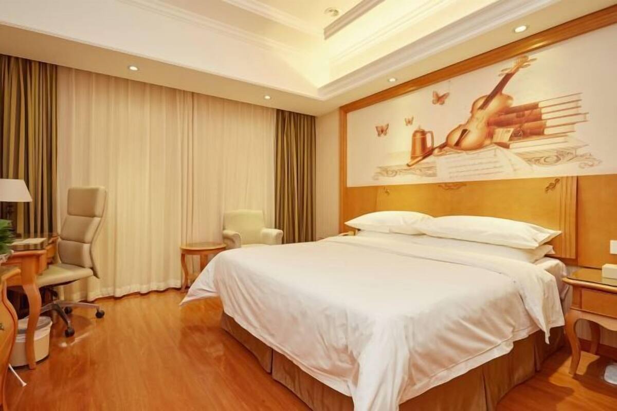 A hotel room with a large bed, a desk, a chair, and a painting on the wall.