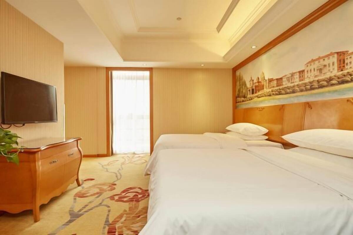 A hotel room with a bed, a television, a dresser, and a painting on the wall.