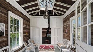 Une véranda couverte, meublée de meubles en osier blancs, avec une table centrale et un lustre décoratif.