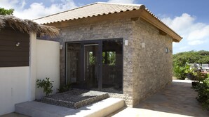 Ein kleines Steinhaus mit Ziegeldach, Glastür und einer kleinen Sitzgelegenheit im Freien.