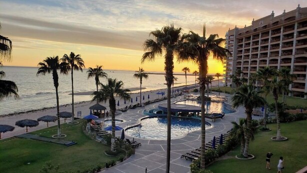 Zwembadgedeelte van een resort met palmbomen, een strand en een hotelgebouw.