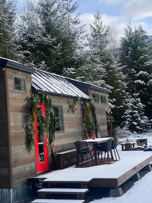 Cozy cabin with a rustic exterior, featuring a red door and a small deck with outdoor dining space.