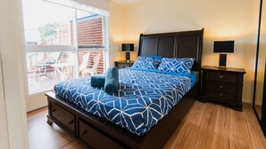 Un dormitorio con una cama grande, dos mesitas de noche con lámparas, una ventana con persianas y vistas a muebles de exterior.