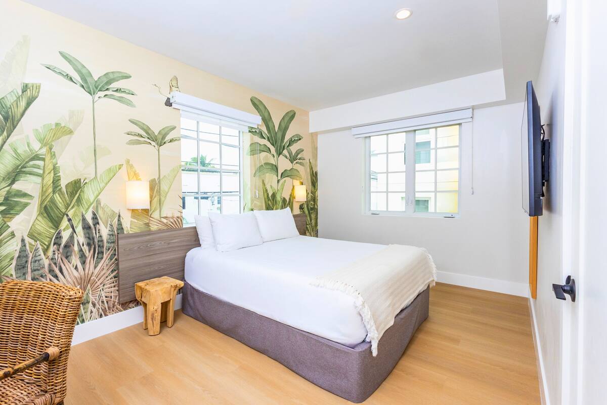 A bedroom with a bed, a wall-mounted TV, and a window.