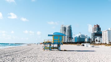 Uma praia com uma torre salva-vidas e edifícios ao fundo.