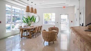 A spacious lobby with a wooden dining table, wicker chairs, and large windows offering views of the outside. - Casa Ocean (Miami Beach)