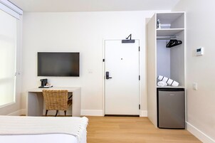 A hotel room with a bed, a desk with a chair, a television, a wardrobe, and a mini-fridge.