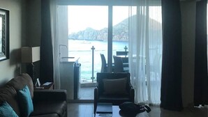 Uma sala de estar com sofá, mesa de centro e vista para o mar através de grandes janelas.