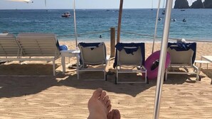Uma praia com cadeiras de praia e guarda-sóis, areia dourada e o mar ao fundo.