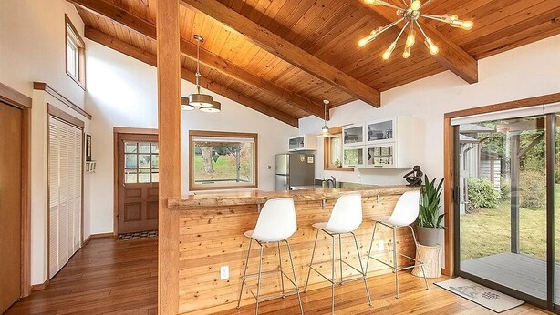 A spacious kitchen with wooden beams, a bar area with white bar stools, and a large sliding glass door leading to a backyard.